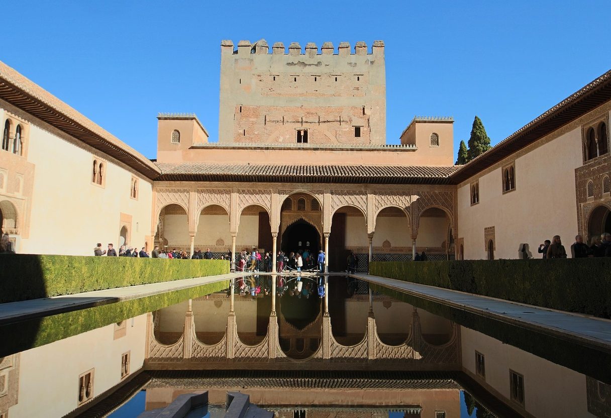 Court of the Myrtles reflecting pool mirroring the arcade and Comares Tower, with myrtle hedges and visitors