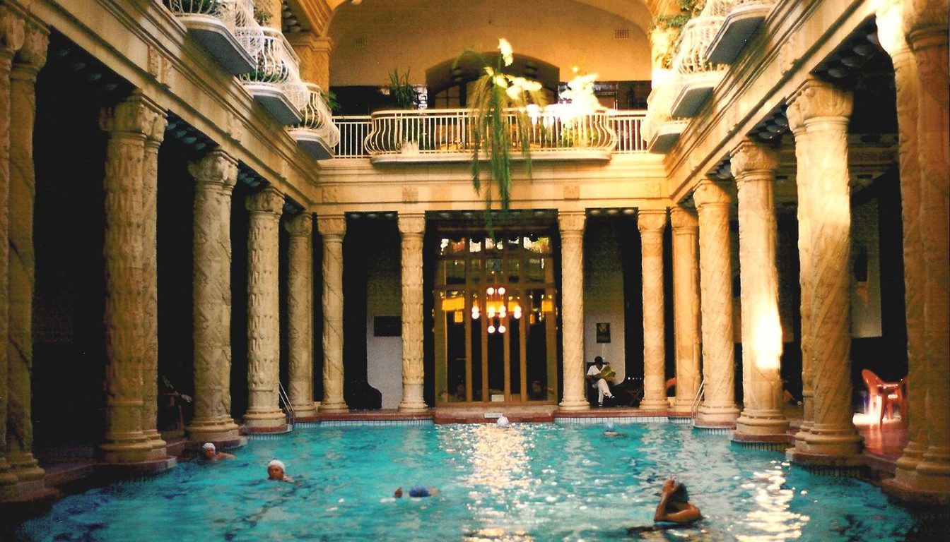 Symmetrical view of the columned indoor swimming pool at the Gellért Baths with balconies and warm lighting