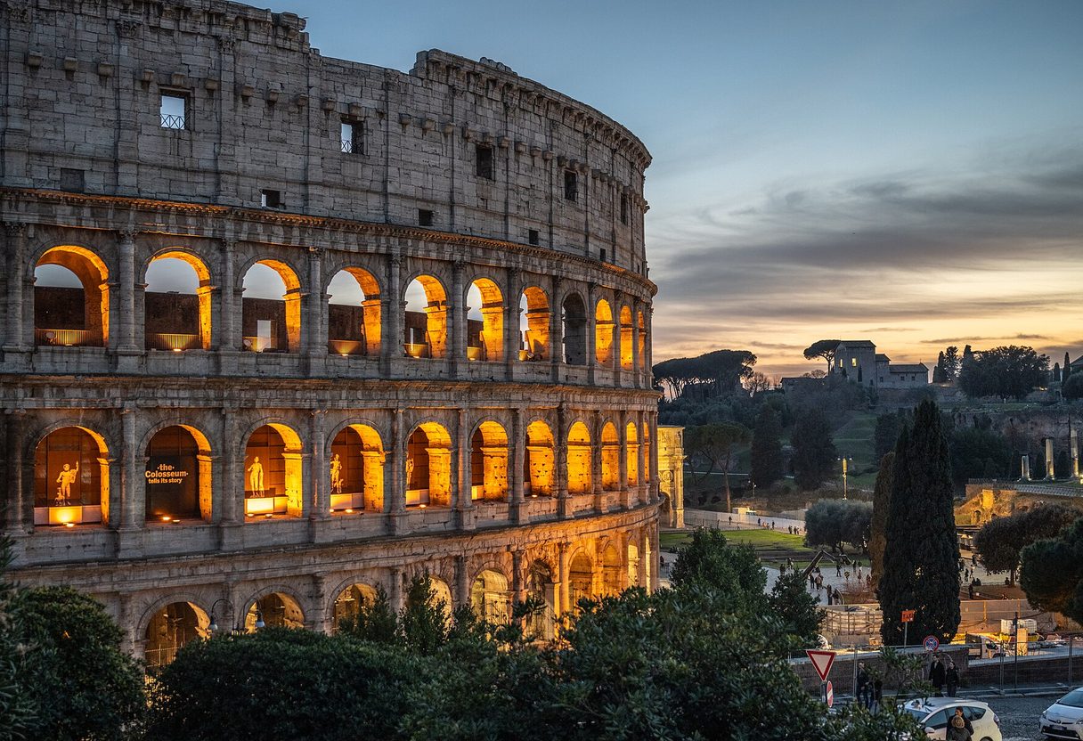 Colosseum at dusk with warmly lit arches against a twilight sky and the Roman Forum beyond