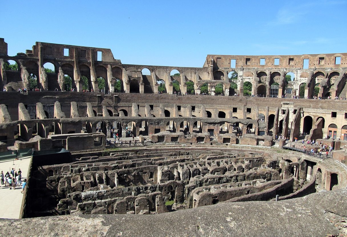 Interior of the Colosseum with exposed hypogeum chambers and tiered arched walls under a clear blue sky