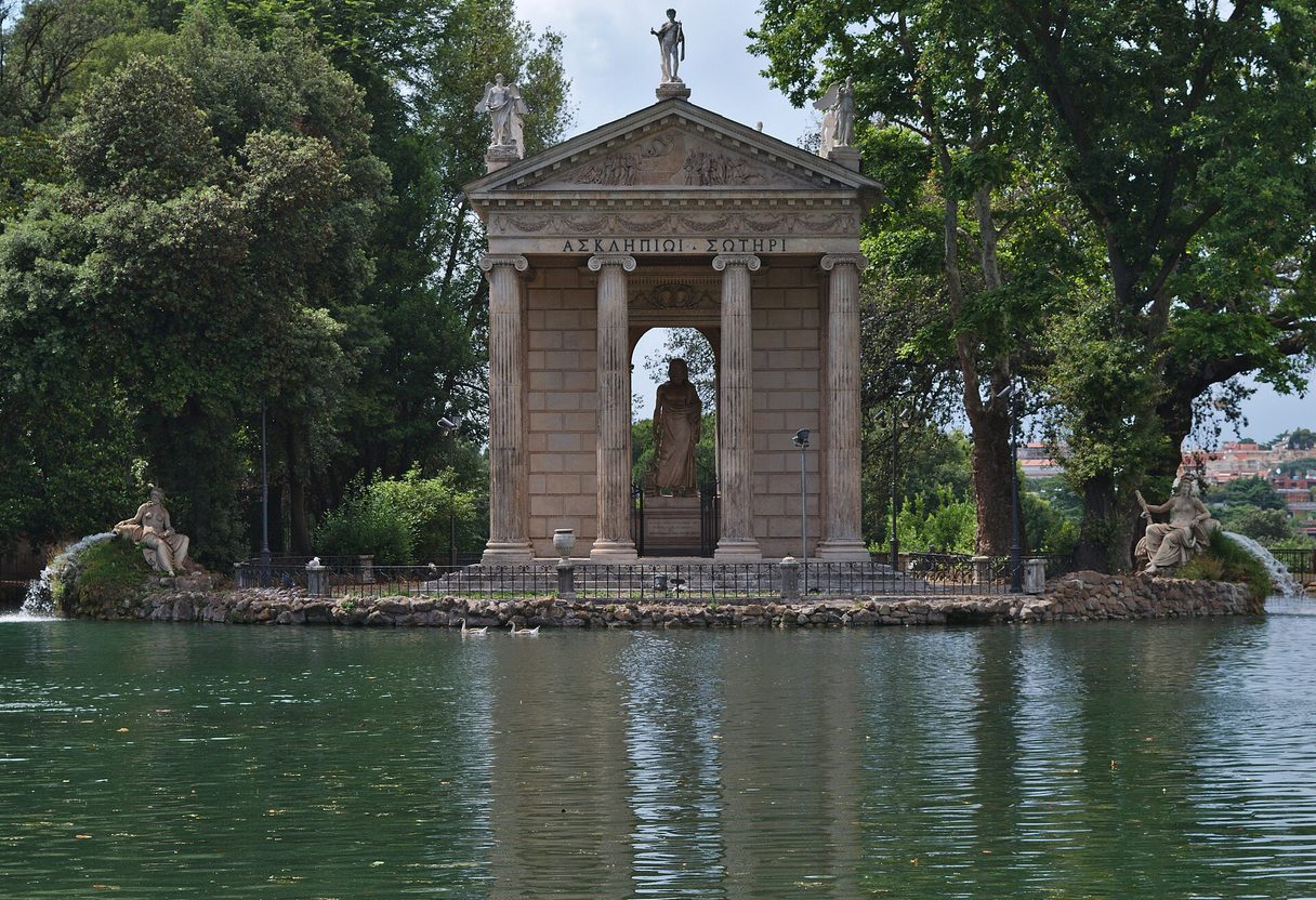 Temple of Asclepius with Ionic columns and statue inside, rising from its island in the Villa Borghese lake