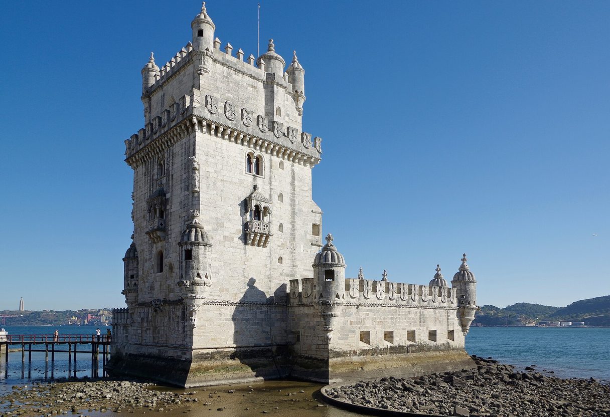 Belém Tower standing on the edge of the Tagus river at low tide under a clear blue sky