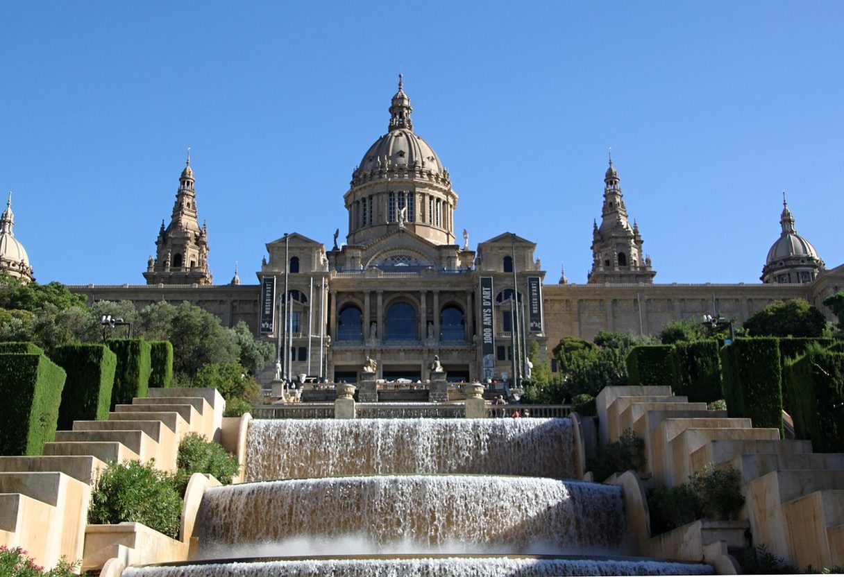 Terraced hedges and cascading fountains below the domed Palau Nacional on Montjuïc under a clear blue sky