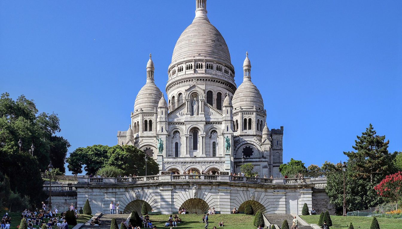 Sacré-Cœur's white domes crowning Montmartre hill above green lawns, stairways and visitors on a sunny day