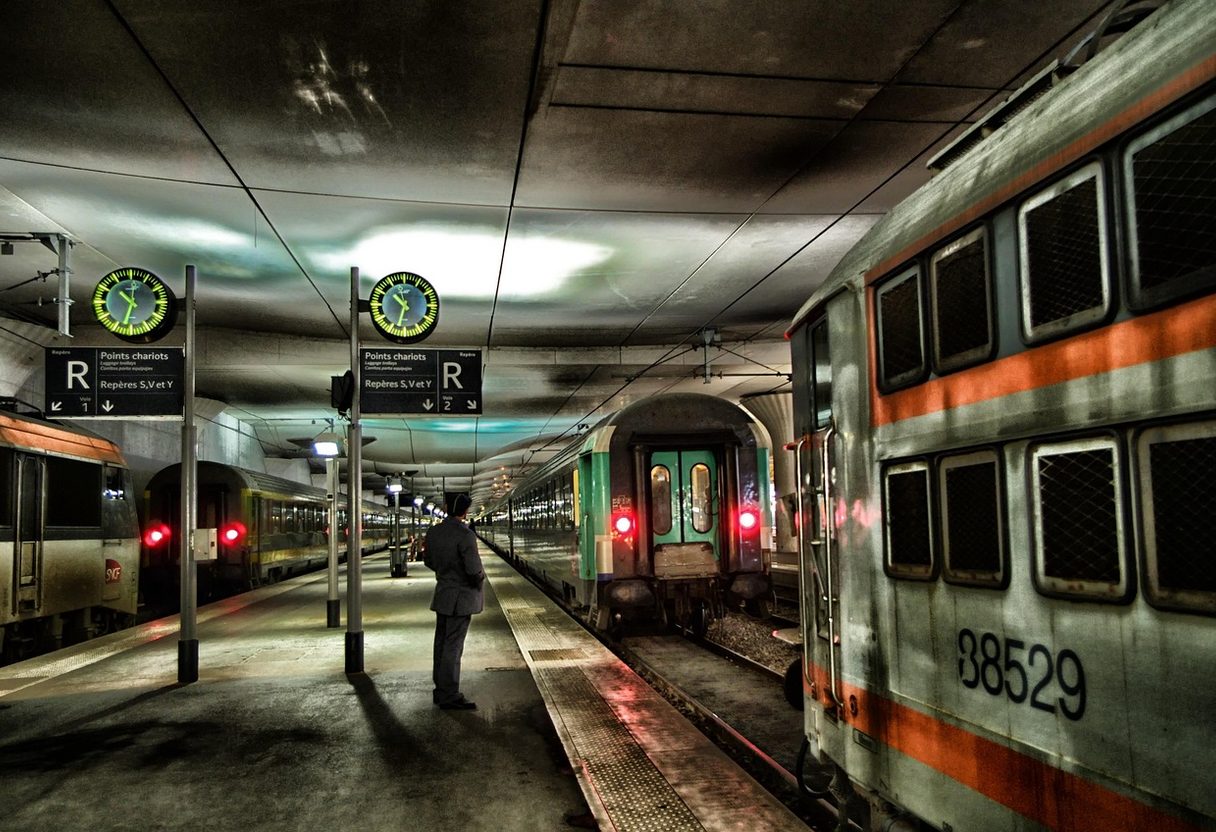 Underground Paris station platform with RER signs, clocks and suburban trains, a lone man waiting between tracks
