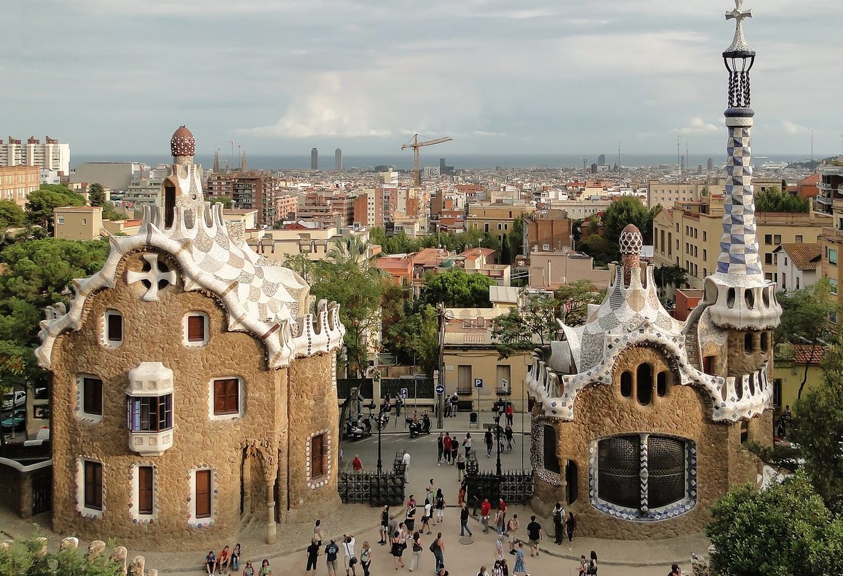 Park Güell's two gingerbread-style gatehouses framing the entrance plaza, with Barcelona's rooftops and the sea behind