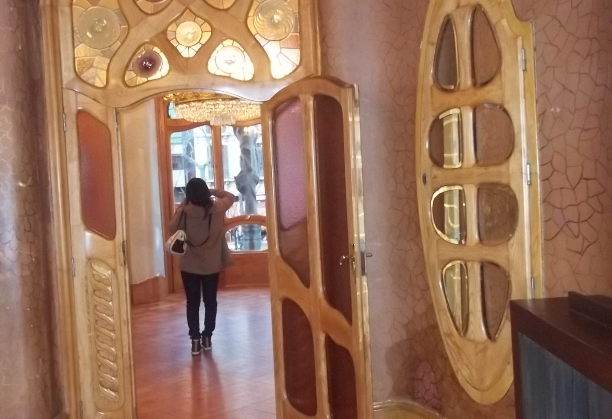Casa Batlló interior with curved wooden doors, round stained glass panes and a visitor walking through