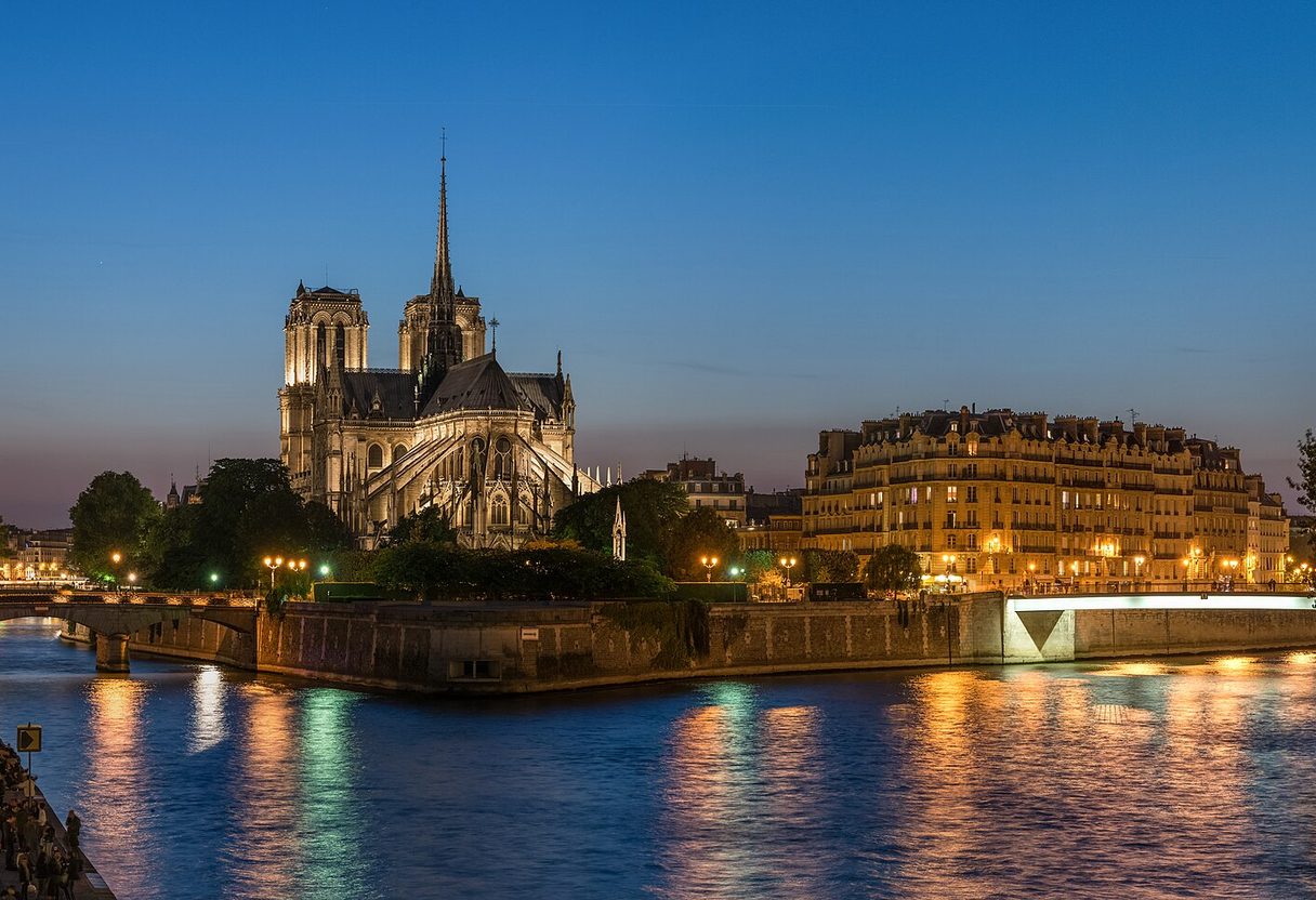 Notre-Dame cathedral and Île de la Cité at dusk, city lights reflecting on the Seine under a deep blue sky