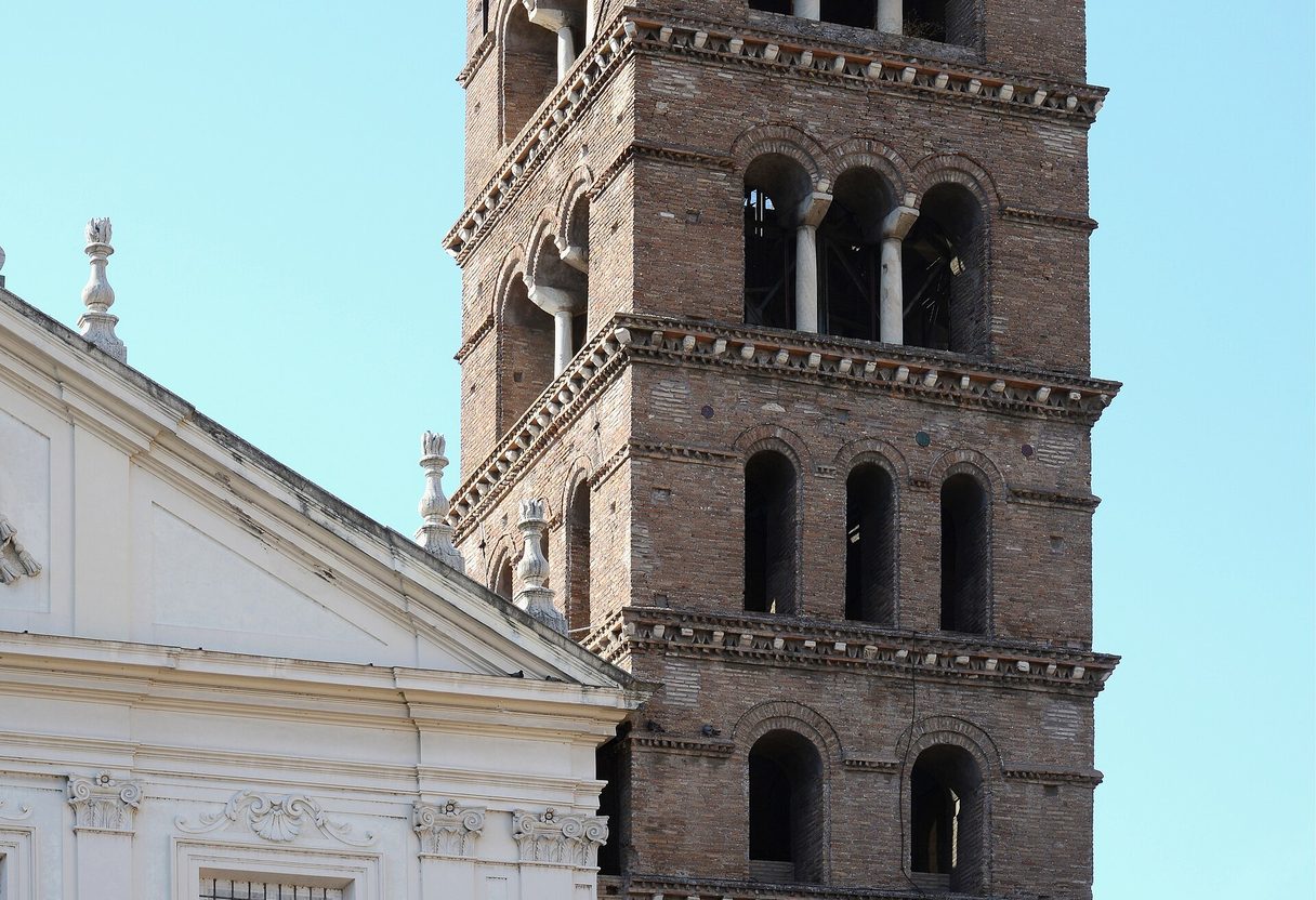 Romanesque brick bell tower rising behind the white facade of Santa Cecilia in Trastevere under a blue sky